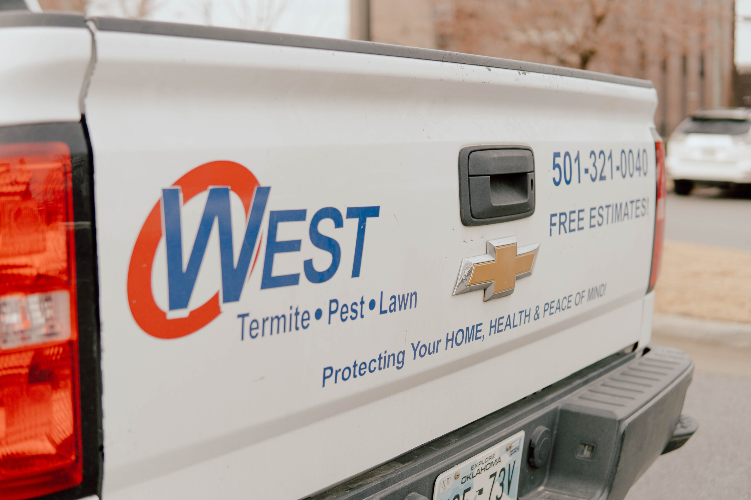 The image shows the side of a white pickup truck with West Termite • Pest • Lawn and a phone number on the door, advertising free estimates, pest control services, and termite inspections for real estate needs.
